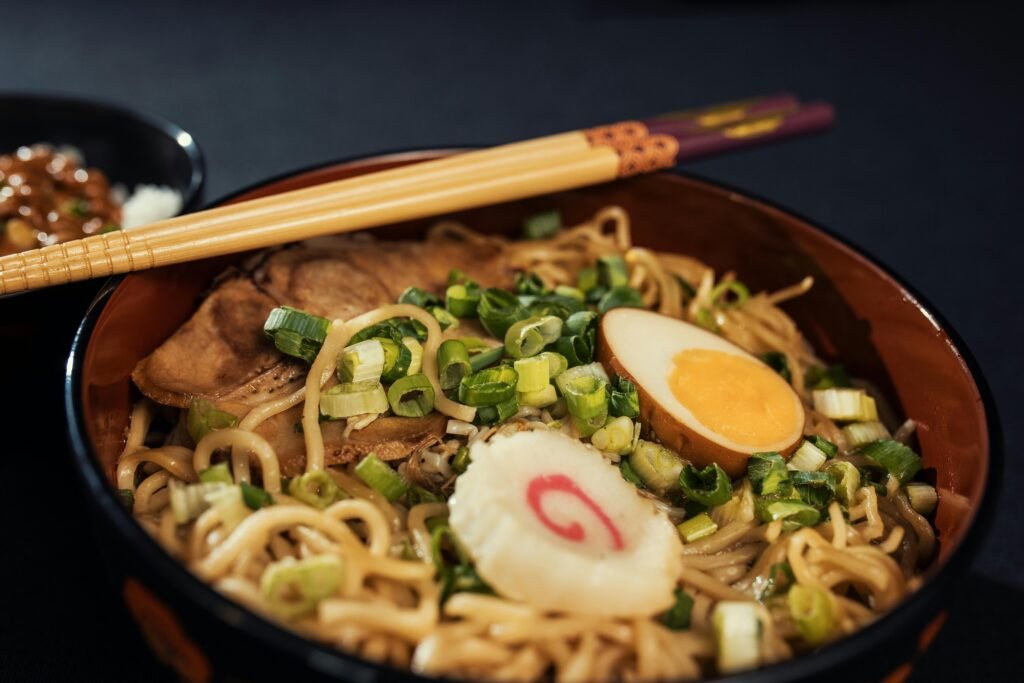 Bowl of traditional Japanese ramen with boiled egg, scallions, and narutomaki served with chopsticks.